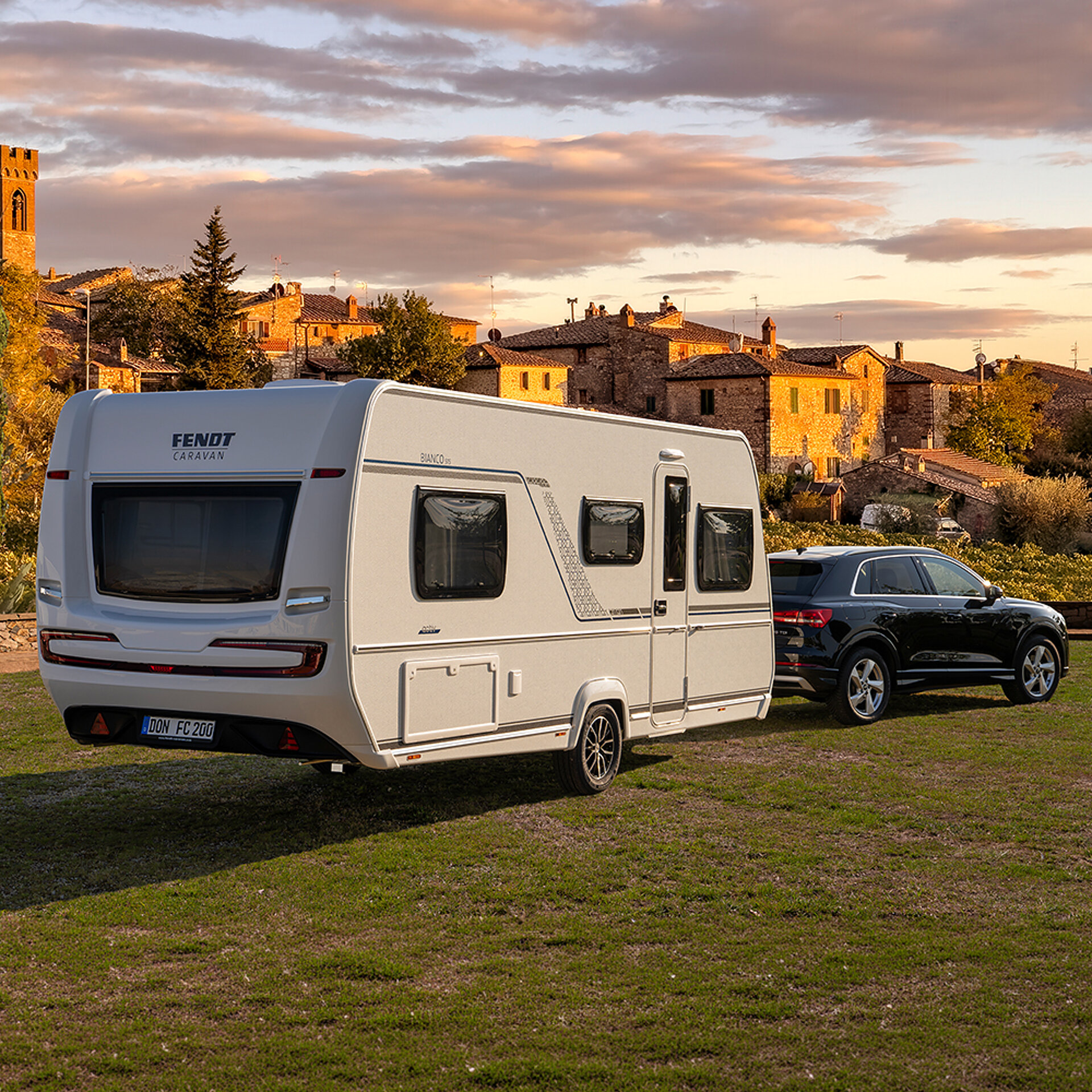 Ein Fendt-Caravan BIANCO parkt auf einer Wiese vor einer malerischen Stadt.