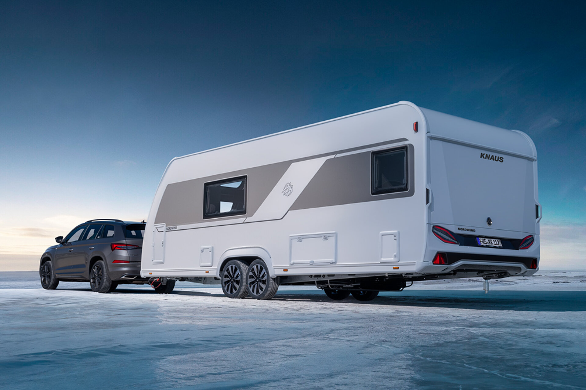 Ein KNAUS Nordwind Wohnwagen wird von einem SUV über eine Eisfläche gezogen.