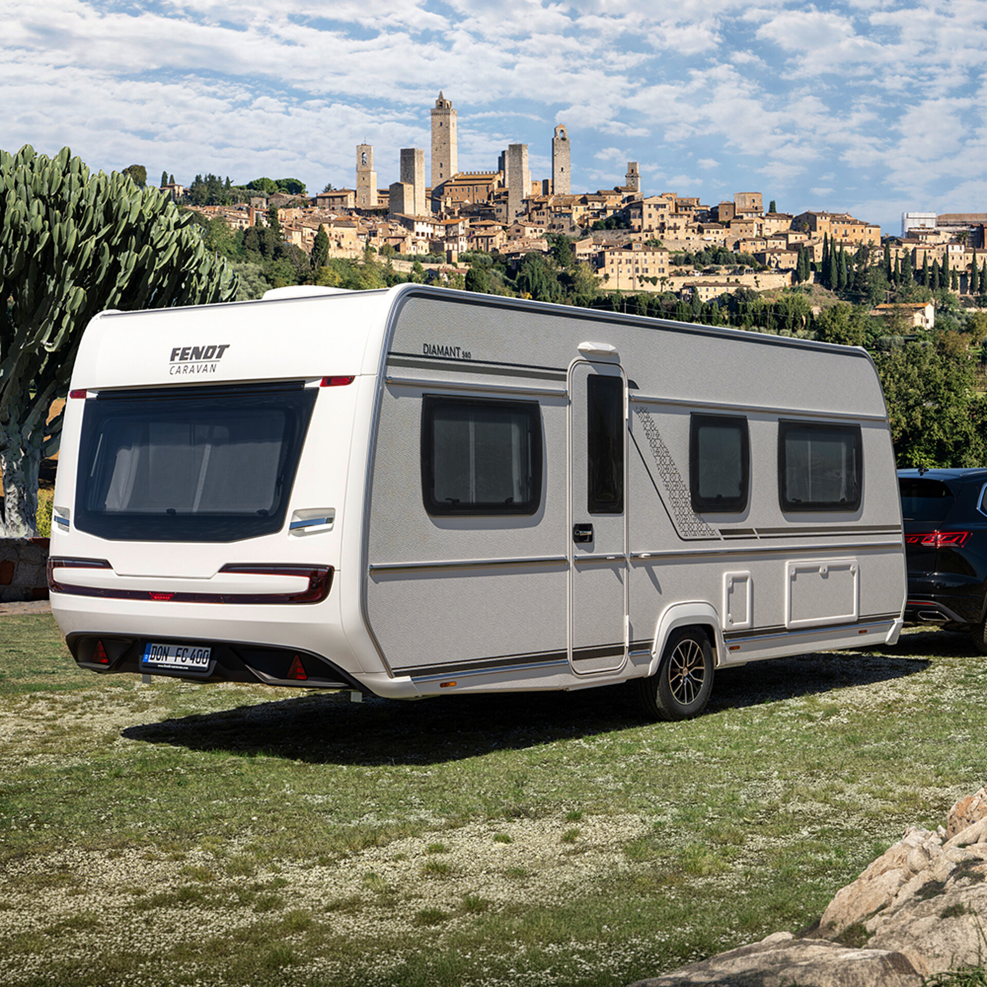 Ein Fendt-Caravan DIAMANT parkt auf einer Wiese vor einer malerischen Stadt.