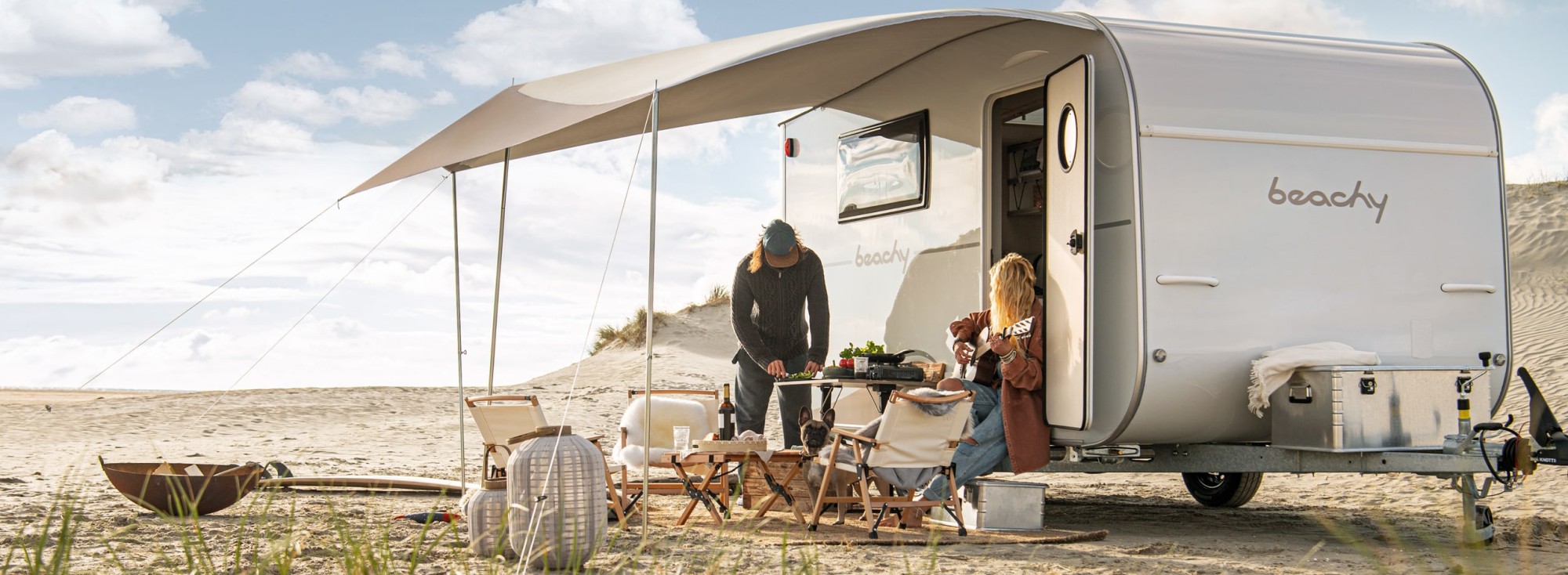 Ein Paar sitzt vor einem BEACHY Caravan am Strand.