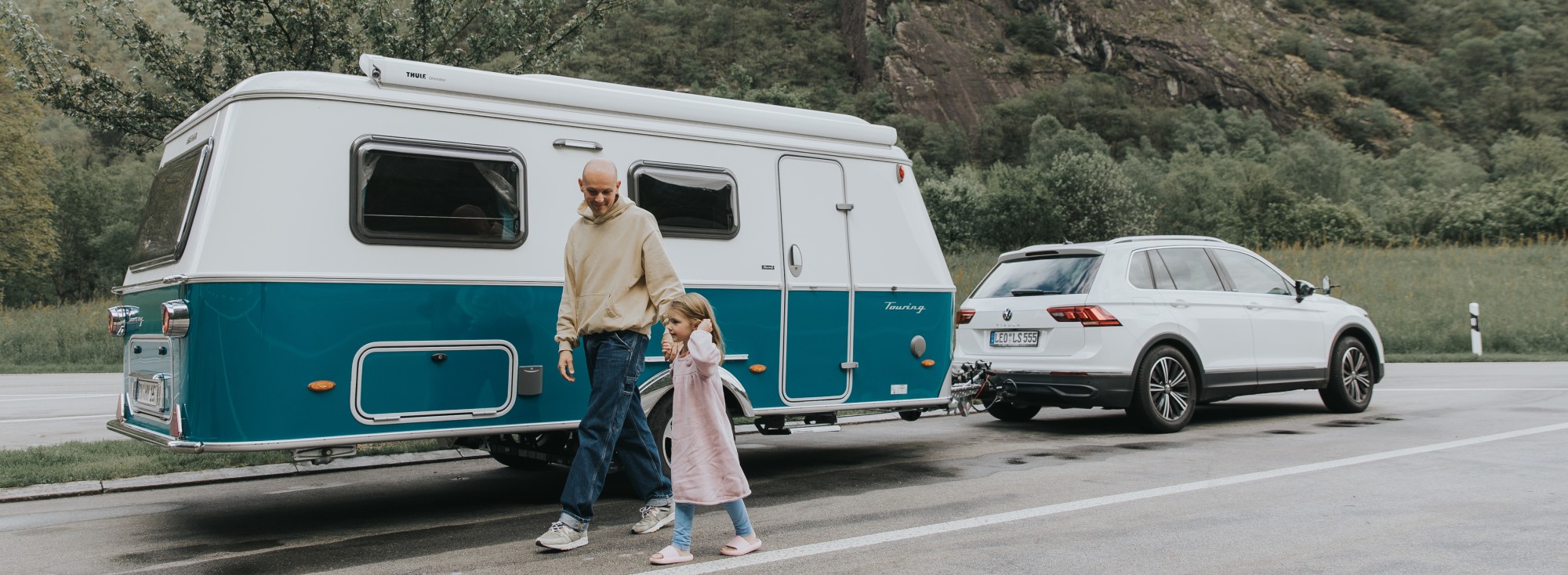 Vater und Sohn laufen vor einem geparkten ERIBA Touring Wohnwagen entlang.