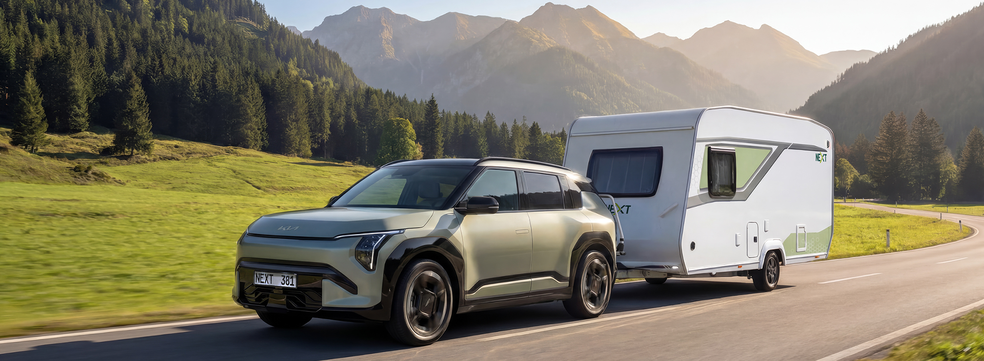 Ein NEXT Wohnwagen wird von einem SUV eine Landstraße entlanggezogen.